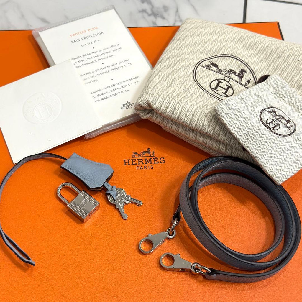 Hermes keychain, keys, and leather strap on an orange Hermes box with a white card.